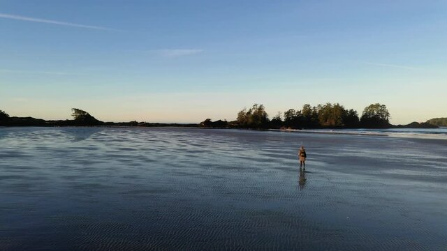 Female Photographer Walking Down An Empty Beach At Dawn
