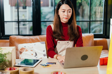 SME small business Asian female entrepreneur or shop owner using computer laptop checking on stock order. woman working for online store at home. management new normal lifestyle