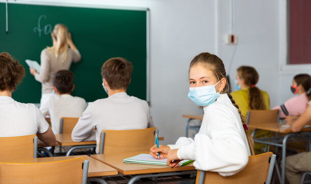 Student in protective mask studying in classroom, listening to lecturer and writing in notebook. High quality photo