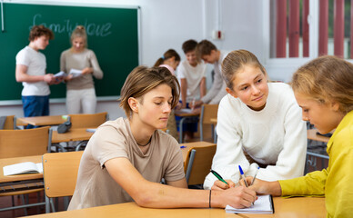 Group of diligent school kids discussing something in group during lesson in classroom in secondary...