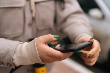 Close-up cropped shot of unrecognizable woman using smartphone to unlock electric scooter standing in city street, selective focus, blurred background.