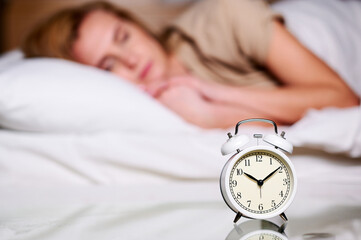 Closeup alarm clock on bedside table with woman sleeping on background