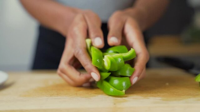 Dark skinned woman's hands placing chopped green peppers next to the rest of the vegetables on a plate. Slow motion, Close up.