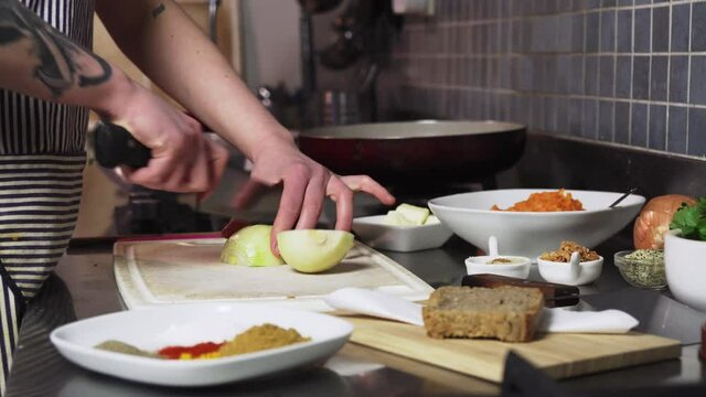 Cutting onion in kitchen, closeup view of hands and knife and foodstuffs around
