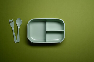 Above view lunch box with spoon and fork on green background.