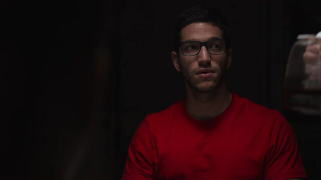 Medium closeup of man wearing red shirt, hands pour bevarage at table, static
