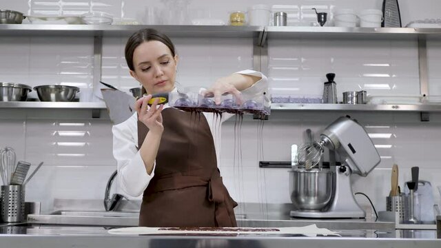 Chef or chocolatier makes sweet chocolates in a professional kitchen. He turns the mold over and pours the rest of the chocolate onto the table.