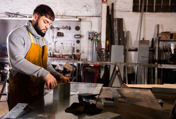 Young bearded man working in industrial workshop, measuring metal structures ..