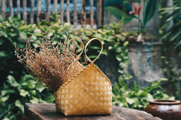 Real nature beauty background. Yellow Bag beach straw with dry flower for decor design outdoor place wood brown table. Tropical green background. Summer trend sun calm mood relaxation, simple day life