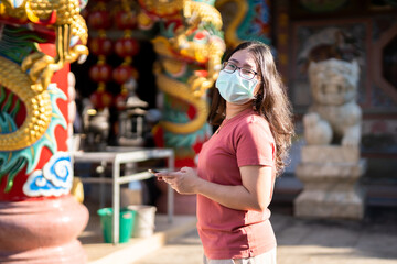 Fototapeta na wymiar Portrait of asian woman traveler wear protective mask germs is looking up information on smartphone at Chinese buddhist temple or shrine,Prevention of the spread of COVID-19 virus,Chinese New Year