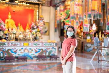 Obraz na płótnie Canvas Portrait of asian woman traveler wear protective mask germs is praying at Chinese buddhist temple or shrine in Thailand,Prevention of the spread of COVID-19 virus,Chinese New Year