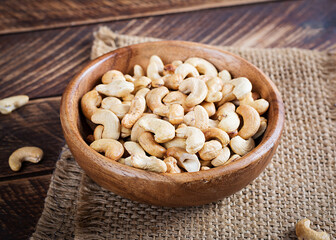 Tasty cashew nuts in bowl on wooden table.