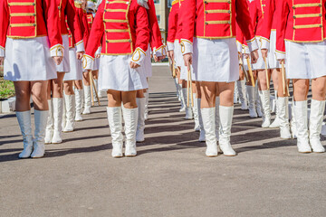 Large group of young girls in red and white ceremonial suits march in formation on a city street. Festive procession of drummers. Front view. - Powered by Adobe