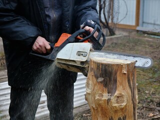sawing a planed stump at an angle using a chainsaw by a worker in a rural courtyard, captured the movement in the process of working with a gasoline saw with a wooden material