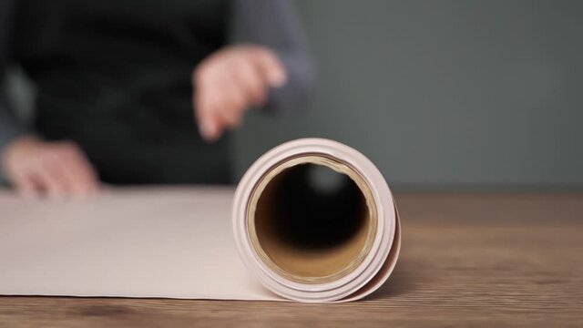 Professional florist hands unroll craft paper on wooden table for wrapping flowers in florist workshop on blurred background close view.