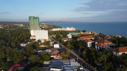 The tallest building of Mui Ne under construction. The developed coastline stretches to the horizon. Many palm trees grow along the road - Powered by Adobe