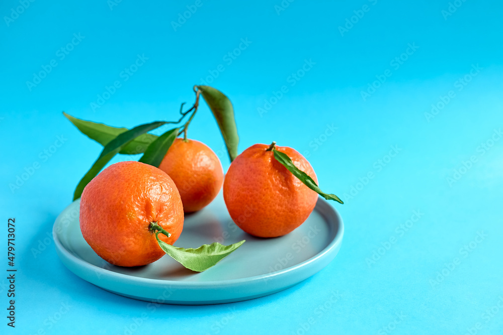 Poster Fresh ripe juicy tangerines with leaves in blue plate on deep blue background. Citrus fruits for healthy eating and natural vitamins. Creative fruit.