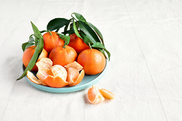 Fresh ripe juicy tangerines with leaves in blue plate on linen tablecloth. Citrus fruits for healthy eating and natural vitamins.