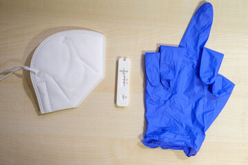 a positive corona rapid test lies next to a medical face mask and a blue medical glove