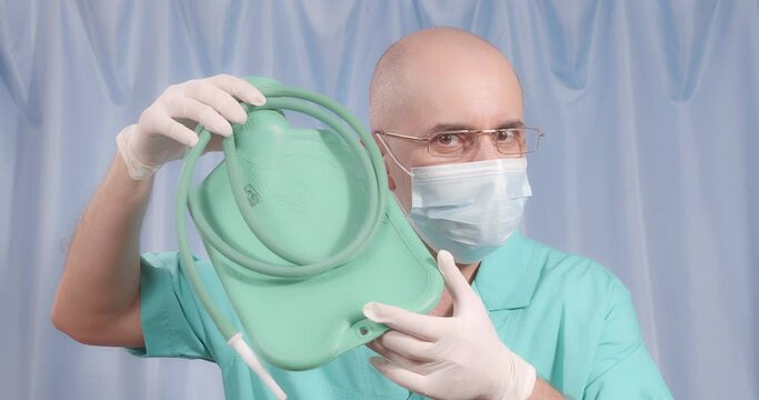 A doctor in a medical mask and rubber gloves shows a large enema.