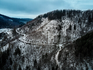 Winding road through mountain covered with forest, winter landscape with curvy highway among countryside, aerial view