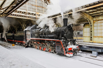 Naklejka premium Retro steam train departs from the railway station. Old vintage steam train on the rail road.
