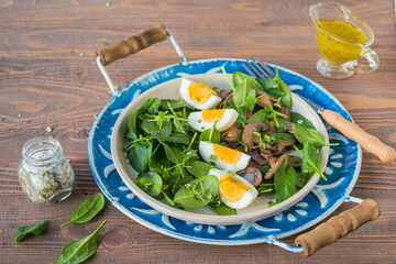 A healthy salad of fresh spinach, fried mushrooms and a boiled egg on a ceramic plate on a wooden background. Salad recipes.
