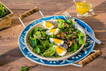 A healthy salad of fresh spinach, fried mushrooms and a boiled egg on a ceramic plate on a wooden background. Salad recipes.