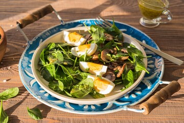 A healthy salad of fresh spinach, fried mushrooms and a boiled egg on a ceramic plate on a wooden background. Salad recipes.