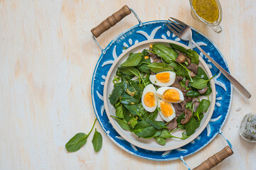 A healthy salad of fresh spinach, fried mushrooms and a boiled egg on a ceramic plate on a wooden background. Salad recipes.
