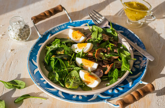 A healthy salad of fresh spinach, fried mushrooms and a boiled egg on a ceramic plate on a wooden background. Salad recipes.