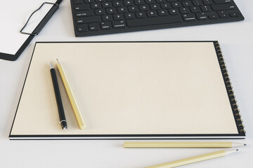 Top view of empty spiral notepad on white table with keyboard and pencils. Drawing, workplace, supplies and art concept. Mock up, 3D Rendering.