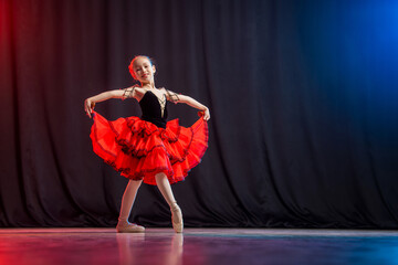 A little girl ballerina is dancing on stage in a tutu on pointe shoes with castanedas, the classic variation of Kitri.