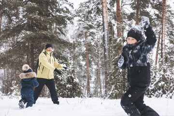 Fototapeta na wymiar Father and sons having fun snowball fight together in winter forest. Happy children playing in snow outdoors. Christmas holidays, New year family vacation. Brothers in warm clothes walking in cold day