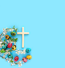 Easter colorful eggs, wooden cross, cherry flowers on blue background. Christian Easter holiday concept. spring festive season. flat lay. copy space
