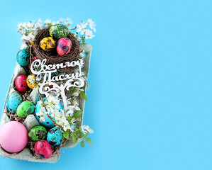 colorful eggs, nest, cherry flowers in cell box on blue background. Happy Easter russian text. Easter holiday concept. spring festive season. copy space