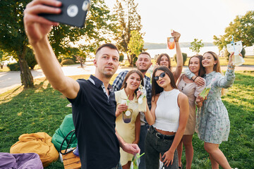 Man taking a selfie. Group of young people have a party in the park at summer daytime