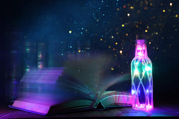 image of mystic bottle with glitter lights next to antique book on wooden table
