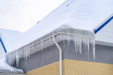 Icicles onroof of private house resulting from improper construction of roof. Metal Downpipe...