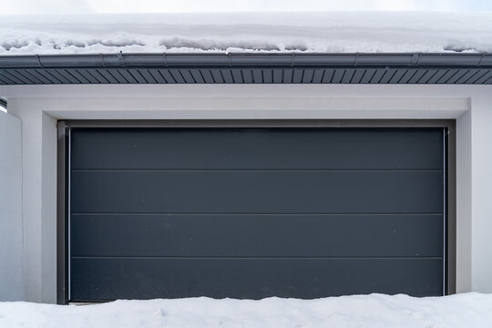 Garage with automatic lifting gray door in a private house with white snowdrift at entrance and roof