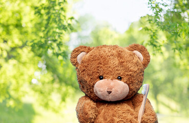 Fototapeta dental care, health and childhood concept - brown teddy bear with toothbrush over green natural background obraz
