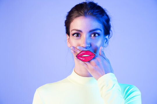 Surprised girl with red paper  lips on neon background. Young woman with the painted lips.