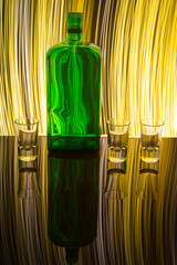 A green bottle with three shot glasses on the background which is illuminated with light painting.