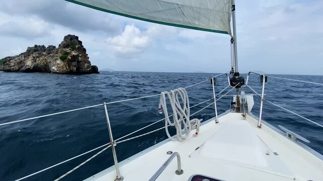 A first person view looking out towards the front of a modern sailboat as it sails through smooth ocean water around the Virgin Islands on a warm summer day in the Caribbean.