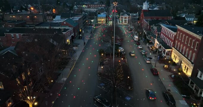 Business storefront buildings on town decorated for Christmas at night. Lights and star as traffic drives.