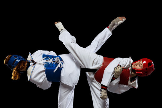Two young women, taekwondo athletes wearing sports uniform practicing isolated over dark background. Concept of sport, skills