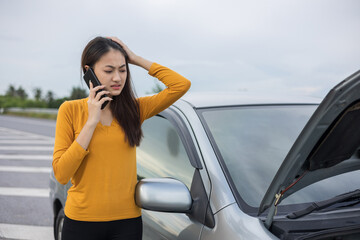 Young asian woman has broken down car on the road she feeling serious and stressed. Look for someone help. Using smartphone Call Emergency assistance or insurance service.