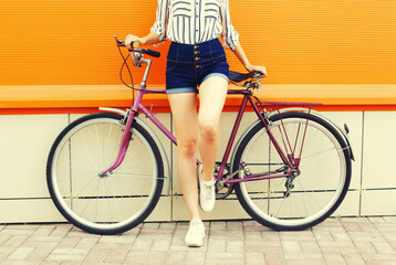 Summer image of legs of beautiful young woman in shorts posing with bicycle in the city on orange background