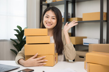 Young beautiful asian entrepreneur stacking the parcel cardboard and hugging product and smile to camera. Happy business woman with many box working at home. Small business owner start up concept.