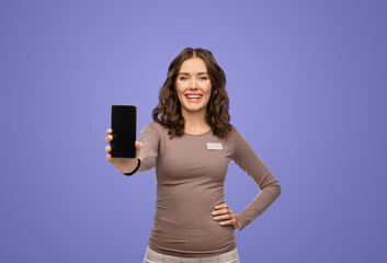 sale, shopping and business concept - happy female shop assistant with name tag showing smartphone over violet background